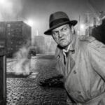 Noir. Gangster Dutch Raccini standing alone at the wharf.